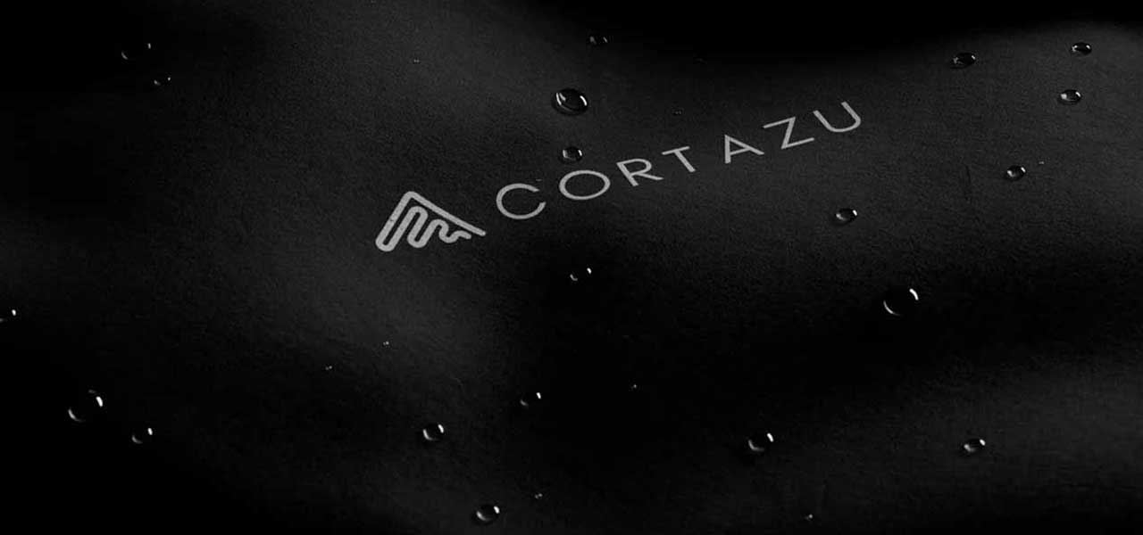Close-up van wind- en waterdichte zwarte stof met Cortazu-logo en waterdruppels.