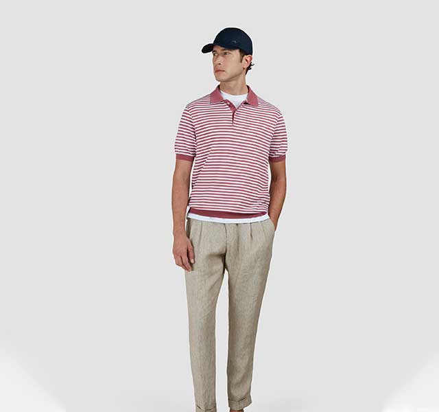Model draagt een Paul & Shark gestreepte polo in roze-wit, gecombineerd met een beige linnen broek.