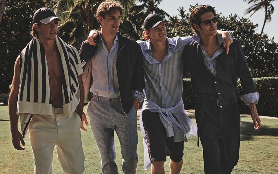 Vier mannen dragen Paul & Shark zomerkleding met nautische invloeden, ontspannen in een stijlvolle maritieme setting.