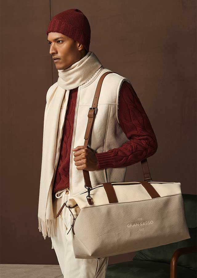 Gran Sasso Accessoirelook – Van den Broek Herenmode Haarlem Man met bordeaux muts en kabeltrui, cream bodywarmer en Gran Sasso weekendtas bij Van den Broek Herenmode in Haarlem.