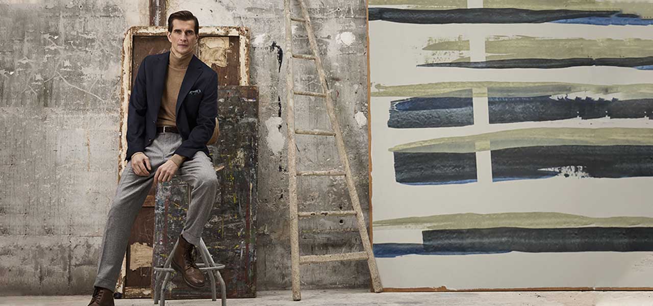 Carl Gross Navy Colbert Look – Van den Broek Herenmode Haarlem Man draagt navy Carl Gross colbert met taupe turtleneck in een kunststudio, gepresenteerd voor Van den Broek Herenmode in Haarlem.